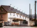 Urocze małe domki szeregowe projekty z białymi kominami i jasnymi fasadami. Srebrny samochód zaparkowany przed ogrodzeniem.