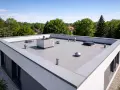 Nowoczesny budynek z płaskim dachem, którego wykończenie zapewnia estetykę i funkcjonalność. Na dachu widoczne są elementy wentylacyjne i świetlik.