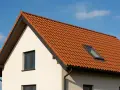 Nowy dach dwuspadowy z dachówką w kolorze cegły, z oknem połaciowym, wieńczy biały dom.