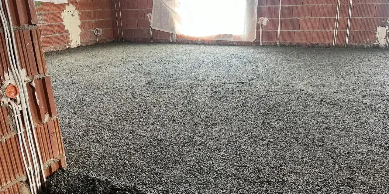 Wylewki styrobeton na podłodze w budowie. Ściany z cegły, okna zasłonięte, widoczne instalacje elektryczne.