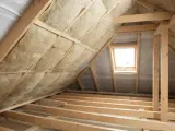 Izolacja poddasza wełną mineralną. Czy 15 cm wełny wystarczy na poddaszu? Widok na drewnianą konstrukcję dachu i okno dachowe.