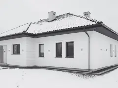 Nowoczesny, biały budynek wolnostojący z dachem pokrytym śniegiem. Wokół domu leży śnieg, tworząc zimową scenerię.