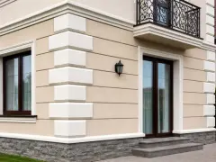Elegancka fasada domu z jasnymi boniami, kamiennym cokołem i ozdobną balustradą balkonu.