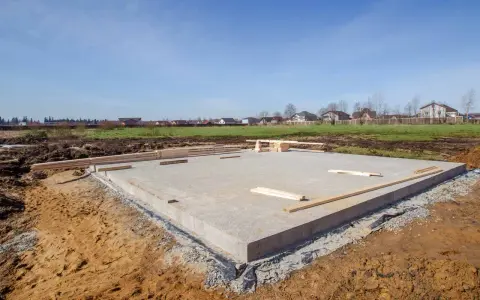 Płyta fundamentowa, jeden z rodzajów fundamentów, gotowa pod budowę domu. W tle domy i błękitne niebo.