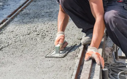 Pracownik wygładza świeży beton, dbając o odpowiednie suchy beton proporcje. Ręce w rękawiczkach trzymają kielnię.