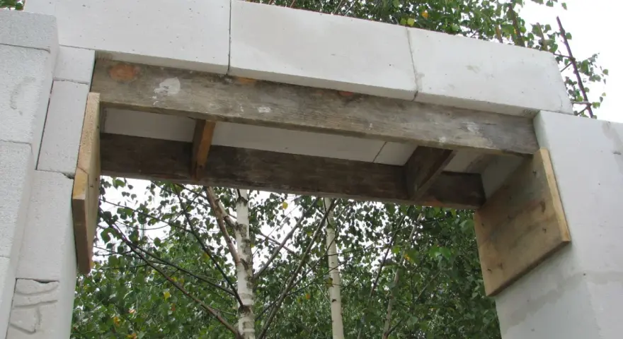 Zbrojenie nadproża 3m z bloczków betonowych, podparte drewnianymi belkami, gotowe do dalszych prac budowlanych.