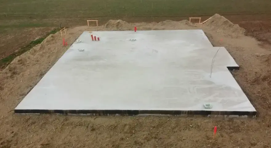 Płyta fundamentowa koszt. Betonowa płyta na budowie, otoczona ziemią i elementami instalacji.