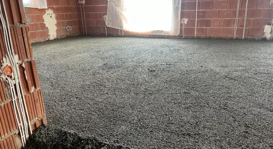 Wylewki styrobeton na podłodze w budowie. Ściany z cegły, okna zasłonięte, widoczne instalacje elektryczne.