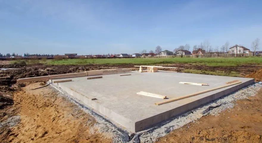 Płyta fundamentowa, jeden z rodzajów fundamentów, gotowa pod budowę domu. W tle domy i błękitne niebo.