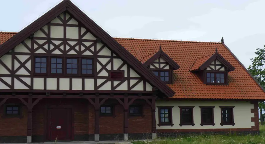 Elewacja budynku w stylu mur pruski, z charakterystyczną drewnianą szachownicą na jasnym tle i ceglanym parterem.