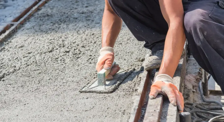 Pracownik wygładza świeży beton, dbając o odpowiednie suchy beton proporcje. Ręce w rękawiczkach trzymają kielnię.