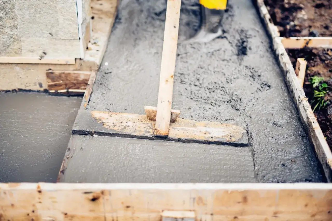 Prace budowlane: świeży beton B20 wylewany w drewnianej formie, przygotowywany do utwardzenia.