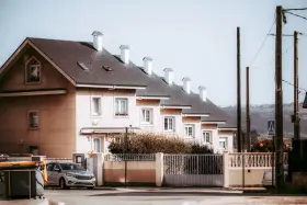 Rząd domów tworzy spójną zabudowę szeregową. Jasne fasady, ciemne dachy i białe kominy tworzą harmonijną całość.