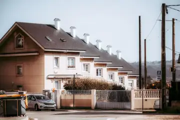 Rząd domów tworzy spójną zabudowę szeregową. Jasne fasady, ciemne dachy i białe kominy tworzą harmonijną całość.